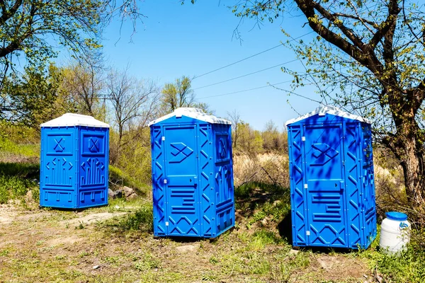 Tres cabinas azules de baños químicos en el parque en el soleado verano — Foto de Stock