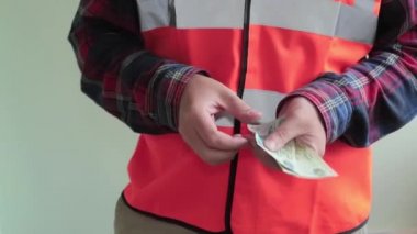 Yansıtıcı yelek giyen adam işçi arap faturaları dirhem ve kameraya para verir sayısı ... Eller closeup açık yeşil arka planda izole.