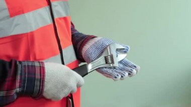 Yansıtıcı yelek giymiş adam işçi, çalışmaya hazırlanıyor, ayarlanabilir anahtarı tutun. Eller closeup açık yeşil arka planda izole.