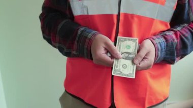 Yansıtıcı yelek giymiş adam işçi kameraya bir dolar banka notu verir. Eller closeup açık yeşil arka planda izole.
