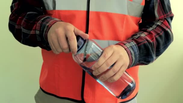 反射ベストを着た男性作業員が開き 飲料水でカメラのペットボトルに与えます 明るい緑色の背景に隔離された手のクローズアップ — ストック動画