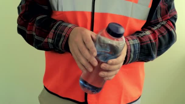 飲料水とカメラのプラスチックボトルに反射ベストを着て働く男 薄緑色の背景に隔離された手を閉じる — ストック動画