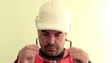 Yansıtıcı yelek ve beyaz kask giymiş Kafkas traşsız adam işçi açık yeşil arka plan üzerinde izole koruyucu çalışma gözlük giyer ... Endüstriyel güvenlik konsepti.