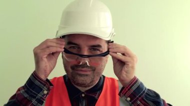 Yansıtıcı yelek ve beyaz kask giymiş Kafkas traşsız adam işçi açık yeşil arka plan üzerinde izole koruyucu çalışma gözlük giyer ... Endüstriyel güvenlik konsepti.