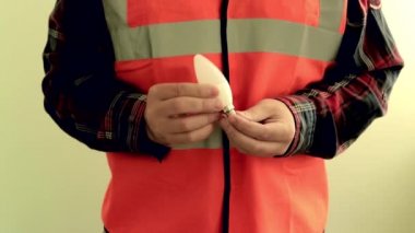 Yansıtıcı yelek giymiş adam elektrikçi kamera enerji tasarrufu Led lamba vermek. Eller closeup açık yeşil arka planda izole.