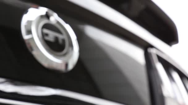 Logo Ford Mustang GT en un coche negro. En un reflejo de un coche de lujo, la gente camina . — Vídeo de stock