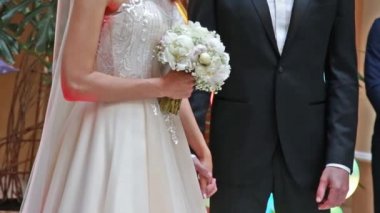 Gelin ve damat bir düğün törenine el tutuyorlar. Beyaz elbise, gül buket tutan kadın.