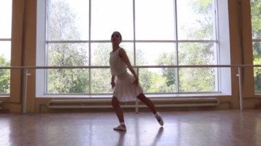 Beyaz elbiseli genç balerin büyük bir pencerenin yanında dans ediyor..