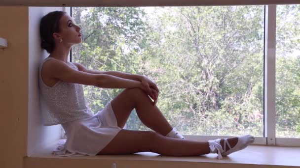 年轻的疲惫的女孩芭蕾舞女坐在窗台上 靠近一个工作室的大窗户 — 图库视频影像