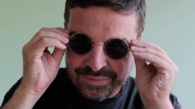 Siyah bir t-shirt ve yeşil yuvarlak Gözlük, Kamera, Showthump Up, Sign Ok arıyorsunuz Gülümseyen Yetişkin Sakallı Adam Portresi. Yalıtılmış Açık Yeşil Arka Plan