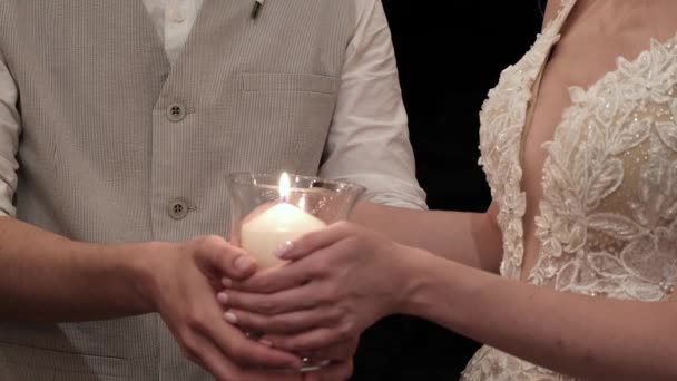 新郎新婦は一緒にレストランで結婚式に燃えるろうそくを保持します 手をクローズアップ — ストック動画