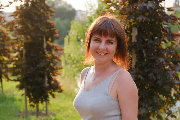 Gün batımında parkta yürüyen 40 yıllık gülümseyen bir kadının portresi.