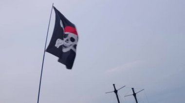 Korsan bayrağı Jolly Roger rüzgarlı bir günde mavi gökyüzü arka plan üzerinde bir gemi direği asılı.