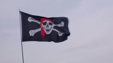 Korsan bayrağı Jolly Roger rüzgarlı bir günde mavi gökyüzü arka plan üzerinde bir gemi direği asılı.
