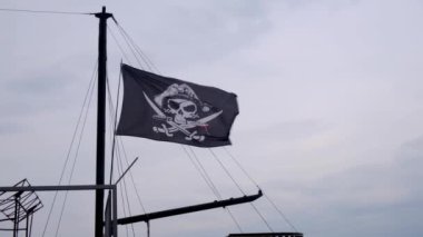 Korsan bayrağı Jolly Roger rüzgarlı bir günde mavi gökyüzü arka plan üzerinde bir gemi direği asılı.