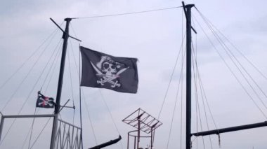 Korsan bayrağı Jolly Roger rüzgarlı bir günde mavi gökyüzü arka plan üzerinde bir gemi direği asılı.