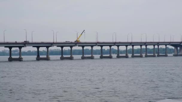 都市の川に架かる大きなコンクリート橋を走る車 トラッククレーンは修理を行います — ストック動画