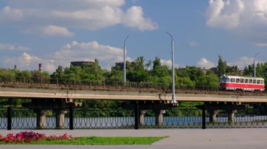 Tramvay, Kryvyi Rih City, Ukrayna 'da yeşil ağaçlar ve mavi bulutlu gökyüzü bir arka planda bir şehirde nehir üzerinde köprü boyunca hareket..