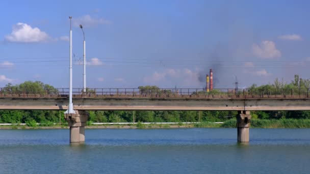 Tram beweegt langs de brug over de rivier op de achtergrond van planten en blauwe bewolkte hemel. — Stockvideo