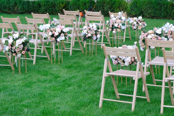 White wooden empty chairs in a row and flowers bouquets on green — Stock Photo, Image