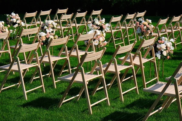 Weiße Holzstühle in einer Reihe und Blumensträuße auf grünem Grund — Stockfoto