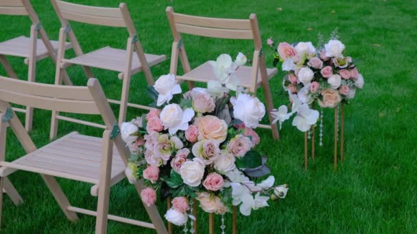 Květinové kytice a bílé dřevěné prázdné židle na zelené trávě. Slavnostní svatební dekorace. — Stock video