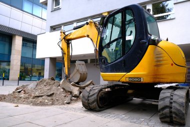 Şehir merkezinde bir Kaldırım üzerinde Sarı Küçük Ekskavatör çalışması.
