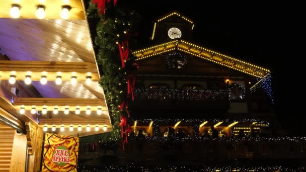 Ludzie odpoczywają, piją grzane wino, na targach noworocznych na balkonie ozdobionym drewnianym budynkiem Christmas Lights. Scena nocna. — Wideo stockowe