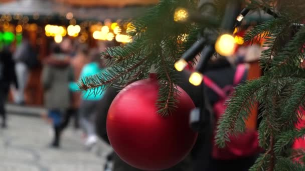 Bola de Natal vermelho na árvore de Ano Novo em uma feira da cidade, pessoas andando por aí . — Vídeo de Stock