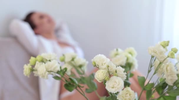 Mujer joven vestida con ropa interior blanca y peignoir acostado en la cama en el dormitorio — Vídeos de Stock