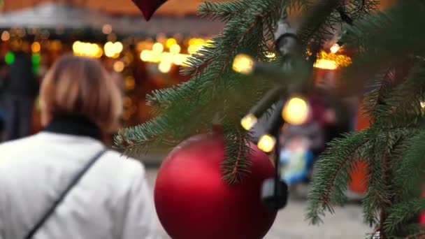 在一个城市的集市上 身着红色圣诞舞会的衣服 在一棵天然的新年树上点亮花环 人群在一座喜庆的城市街道上散步 没有雪 — 图库视频影像