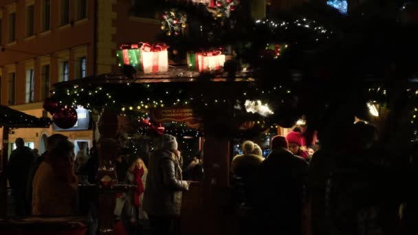 Personas descansando, beber vino caliente, en el mercado de Navidad en la calle de la ciudad nocturna. — Vídeos de Stock