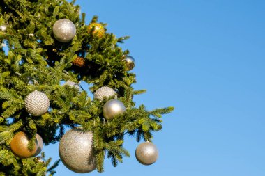 Güneşli yaz gününde mavi bir arka planda sahte Noel ağacının dalları üzerinde altın ve beyaz yeni yıl süslemeleri ve çelenkler. İnsan yok, kar yok. Boşluğu kopyala.
