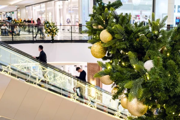Altın Noel topları ve süslenmiş bir köknar ağacının üzerindeki çelenk Alışveriş Merkezi 'nde. Bulanık insanlar yürüyen merdivende, şenlikli iş merkezinde yeni yıl alışverişi yapıyorlar.,.