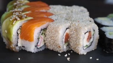 Siyah arka planda dönen masada ton balığı, somon, salatalık ve avokado ile suşi rulosu. Restoranda Japon yemeği çeşitleri.
