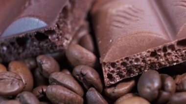 Koyu kavrulmuş kahve çekirdekleri ve çikolataya yakın çekim. Aromatik kahve taneleri ve tatlı çikolata parçaları dönüyor..