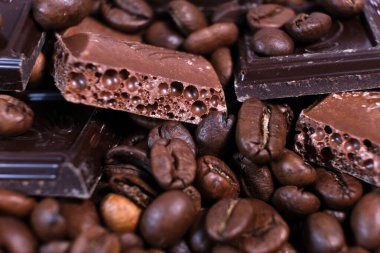 Koyu kavrulmuş kahve çekirdekleri ve çikolata arkaplanından yakın çekim. Aromatik kahve taneleri ve tatlı çikolata parçaları makro fotoğrafçılık, tarlanın derinliği.