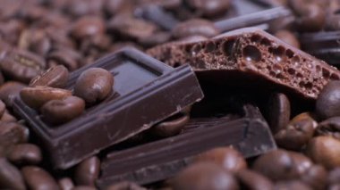Koyu kavrulmuş kahve çekirdekleri ve çikolata yakın plan. Aromatik kahve taneleri ve tatlı çikolata parçaları dönüyor..