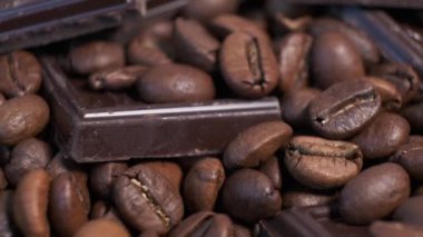 Koyu kavrulmuş kahve çekirdekleri ve çikolata yakın plan. Aromatik kahve taneleri ve tatlı çikolata parçaları dönüyor..