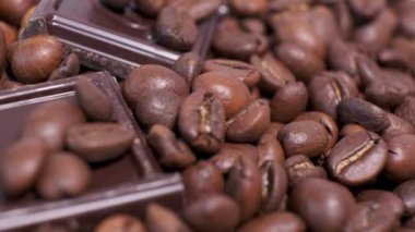 Koyu kavrulmuş kahve çekirdekleri ve çikolata yakın plan. Aromatik kahve taneleri ve tatlı çikolata parçaları dönüyor..