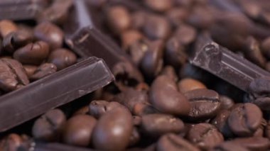 Koyu kavrulmuş kahve çekirdekleri ve çikolata yakın plan. Aromatik kahve taneleri ve tatlı çikolata parçaları dönüyor..