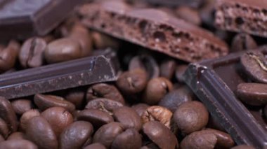 Koyu kavrulmuş kahve çekirdekleri ve çikolata yakın plan. Aromatik kahve taneleri ve tatlı çikolata parçaları dönüyor..