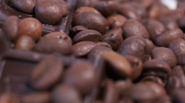 Koyu kavrulmuş kahve çekirdekleri ve çikolata yakın plan. Aromatik kahve taneleri ve tatlı çikolata parçaları dönüyor..