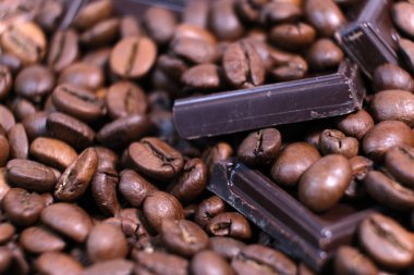 Koyu kavrulmuş kahve çekirdekleri ve çikolata arkaplanından yakın çekim. Aromatik kahve taneleri ve tatlı çikolata parçaları makro fotoğrafçılık, tarlanın derinliği.