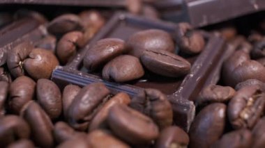 Koyu kavrulmuş kahve çekirdekleri ve çikolata yakın plan. Aromatik kahve taneleri ve tatlı çikolata parçaları dönüyor..