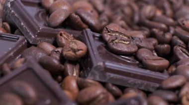 Koyu kavrulmuş kahve çekirdekleri ve çikolata yakın plan. Aromatik kahve taneleri ve tatlı çikolata parçaları dönüyor..