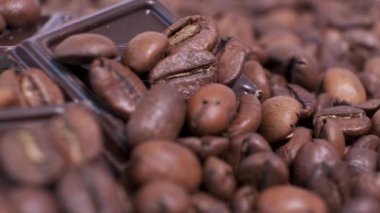 Koyu kavrulmuş kahve çekirdekleri ve çikolata yakın plan. Aromatik kahve taneleri ve tatlı çikolata parçaları dönüyor..