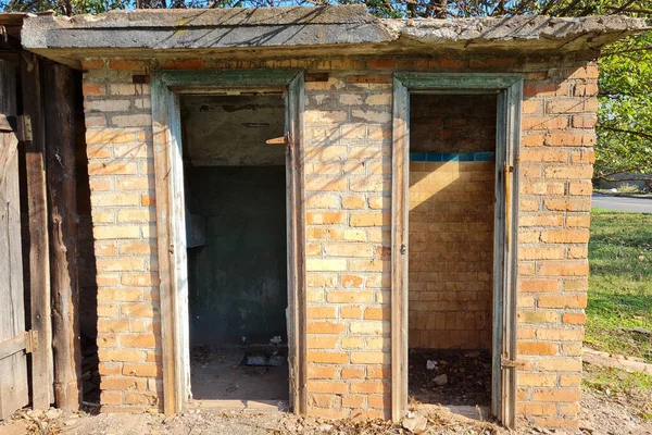 阳光明媚的夏日 有两扇门的废弃旧砖瓦马桶 — 图库照片