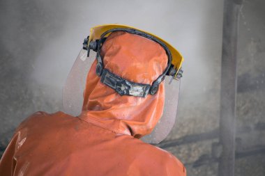 İşçi turuncu koruyucu kıyafetli korozyon hasarlı beton köprü ayağı yüksek basınçlı yıkayıcı ile temizler.