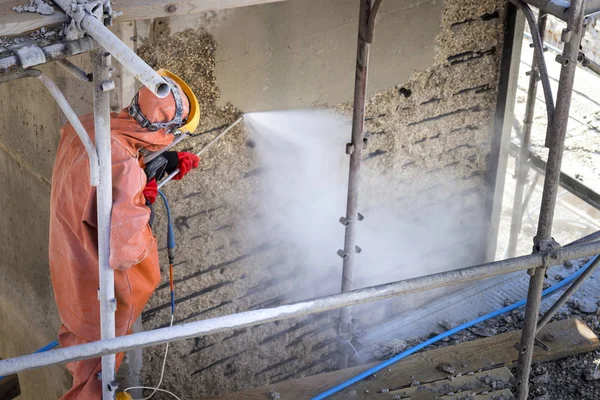 Worker Orange Protective Suit Cleans Corrosion Damaged Concrete Bridge Pillar — Stock Photo, Image